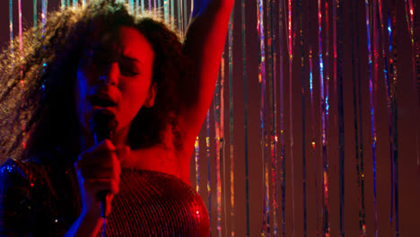 Young-Woman-With-Microphone-Singing-At-Karaoke-Nightclub-Bar-Or-Disco-With-Sparkling-Lights-In-Background-2